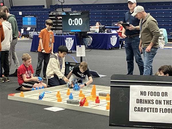 A student adjusts a robot on a competition field.